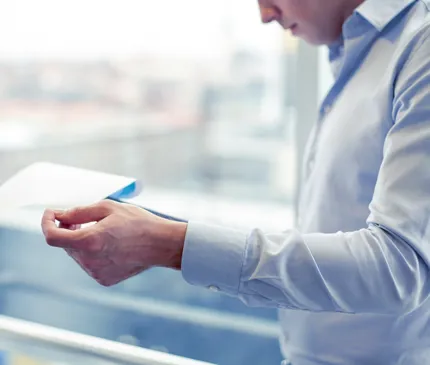 man in blue business shirt looking over a strategic assessment disclosure log in high rise office with blurry backrgound