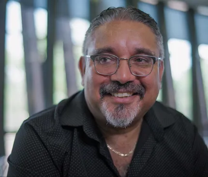 Professor Reuben Bolt Portrait smiling with black shirt, gold necklace and glasses