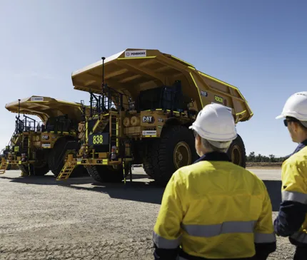 Pembroke Olive Downs Steelmaking Coal Project Two Workers Inspecting Large Orange Mining Truck on Olive Downs Steelmaking Coal Project